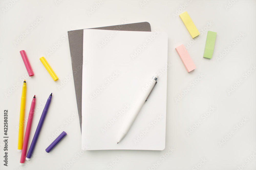 Notepad on a white background with colored pencils and felt-tip pens, rulers and scissors. The notebook lies on a plain background with space for writing. Composition of writing to-dos for the day. Notepad on a white background with colored pencils and felt-tip pens, rulers and scissors. The notebook lies on a plain background with space for writing. Composition of writing to-dos for the day.