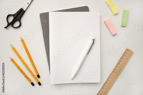 Notepad on a white background with colored pencils and felt-tip pens, rulers and scissors. The notebook lies on a plain background with space for writing. Composition of writing to-dos for the day.