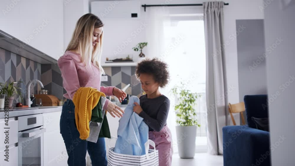Mother with small daughter doing the laundry in kitchen at home.