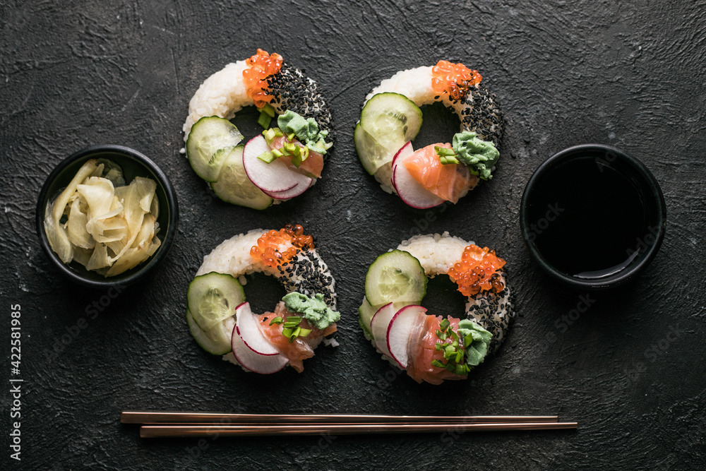 Sushi donuts with salmon, cucumber and radish on dark background top view. Hybrid Foods. Sushi donuts with salmon, cucumber and radish on dark background top view. Hybrid Foods.