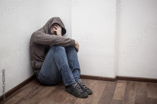 desperate young drug addict wearing hood and sitting alone in corner