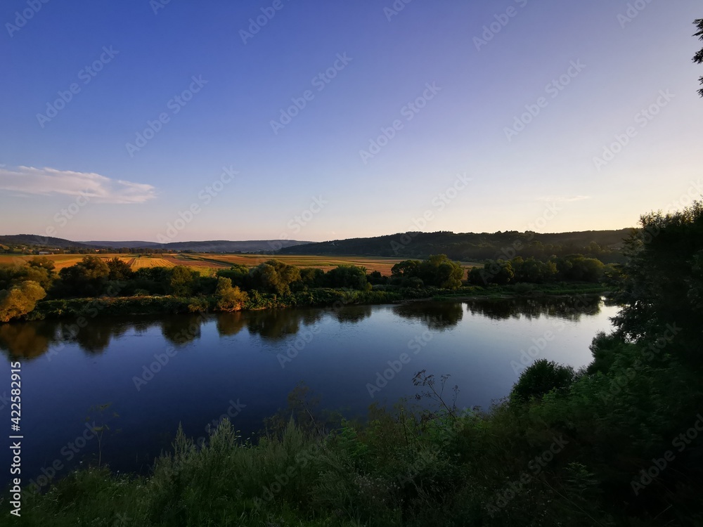 Peaceful river landscape during sunset with strong reflections of nature in water's surface. Clear sky
