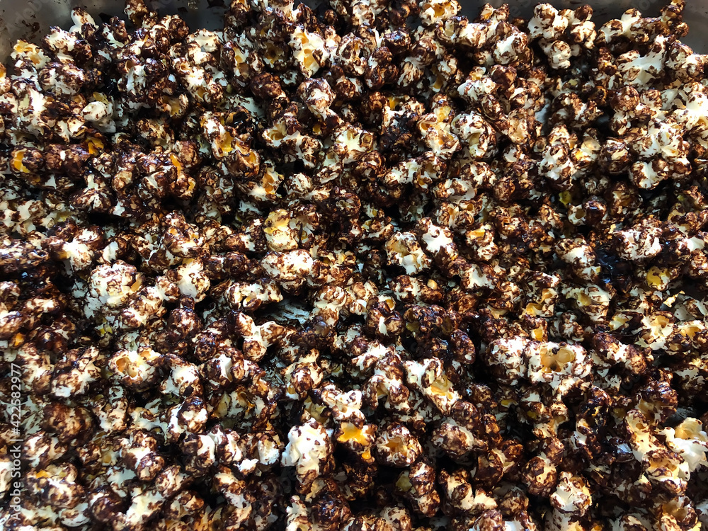 Pouring caramelized chocolate salsa into the popcorn. Making sweet popcorn. Pouring caramelized chocolate salsa into the popcorn. Making sweet popcorn.