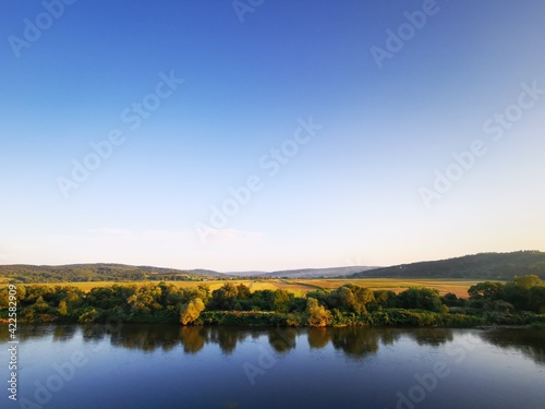 Peaceful river landscape during sunset with strong reflections of nature in water's surface. Clear sky