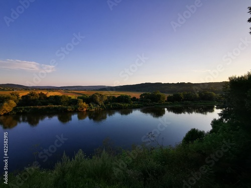 Fototapeta Naklejka Na Ścianę i Meble -  Peaceful river landscape during sunset with strong reflections of nature in water's surface. Clear sky