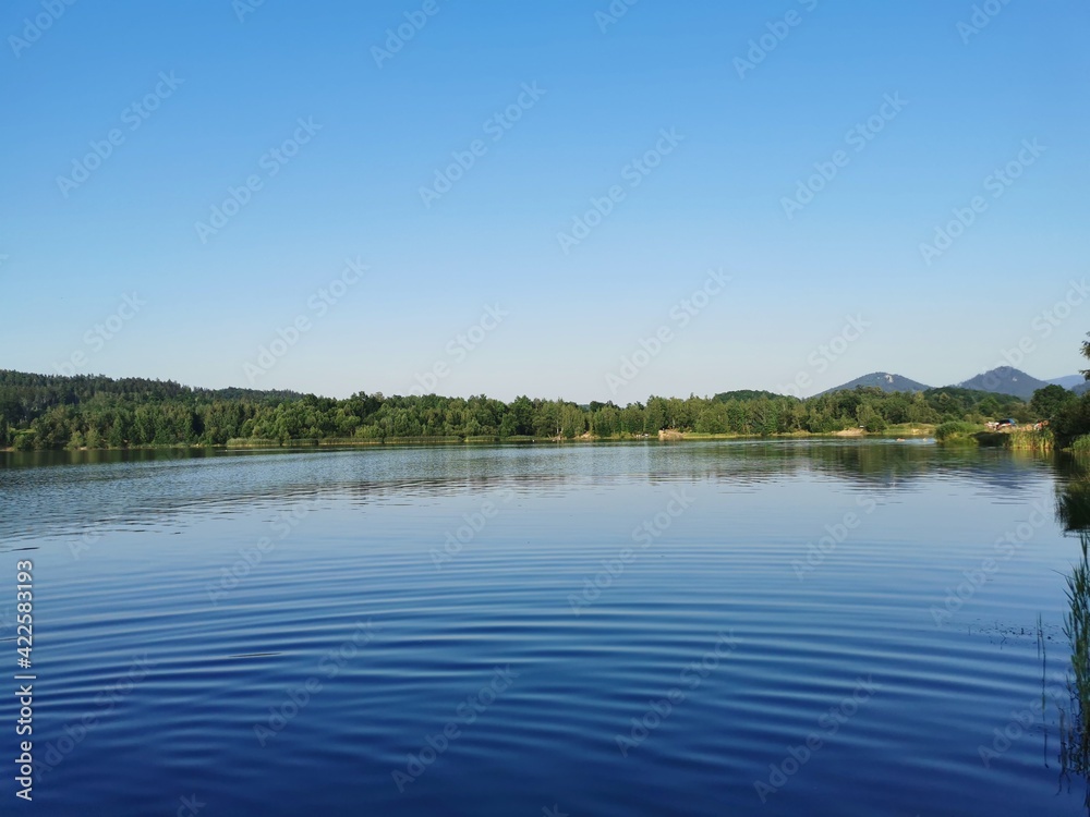 Ripples on blue water surface with trees reflecting in the lake. Clear sky, calm sunset background