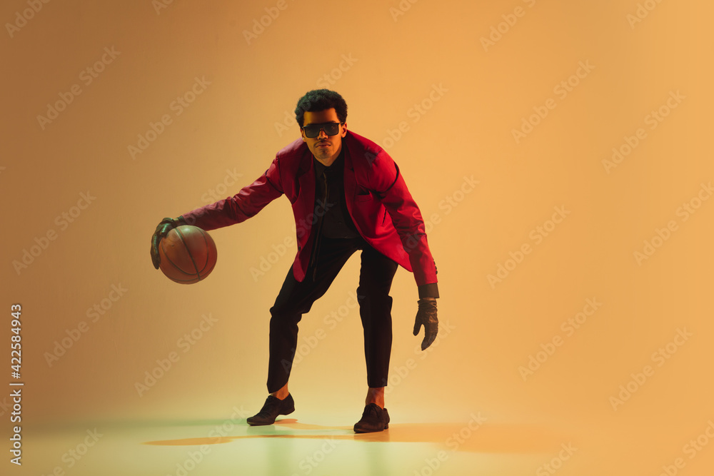 High-fashion styled man in red jacket playing basketball isolted over brown background