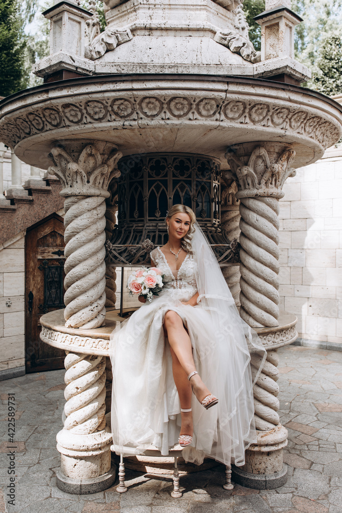 The bride is holding a bouquet of roses. Portrait of the bride against the background of a stone building. Beautiful wedding bouquet.