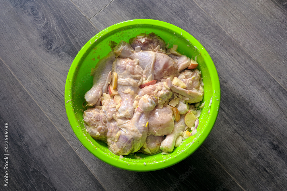 Raw chicken legs in a green plate on a gray parquet background, juicy barbecue with seasoning Raw chicken legs in a green plate on a gray parquet background, juicy barbecue with seasoning