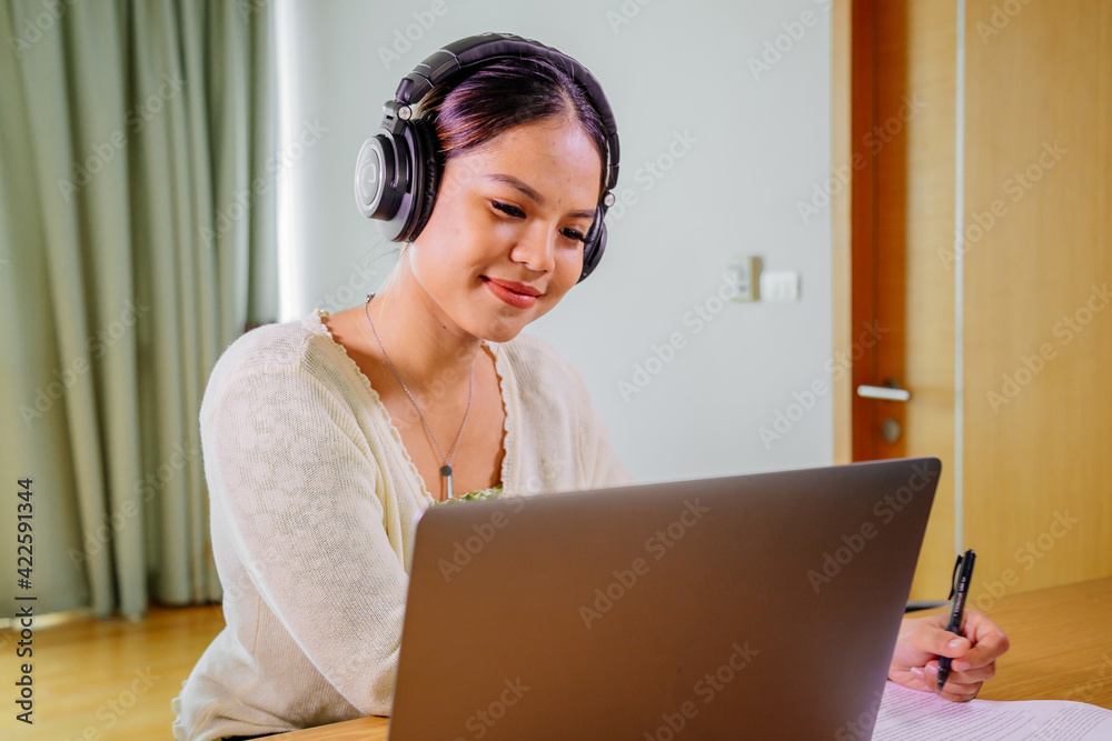 Beautiful young smiling asian woman working on laptop in living room at home. Asia business woman working in her home office. Enjoying time at home. Beautiful young smiling asian woman working on laptop in living room at home. Asia business woman working in her home office. Enjoying time at home.