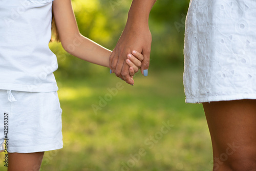 Mother leads her kid in summer forest nature outdoor. Trust, family, protection and help concept. Female and child's hands closeup against the background of summer greenery. 