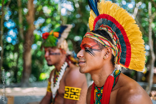 two Indians from the Pataxó tribe. Brazilian Indian from southern Bahia with feather headdress, necklace and traditional facial paintings looking to the left photo