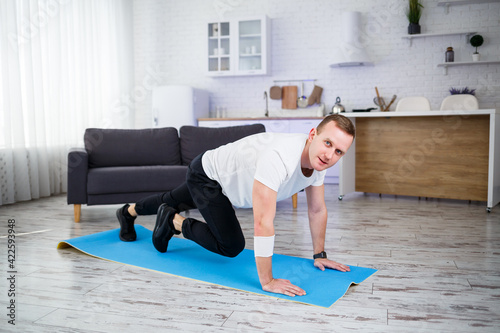 Handsome muscular man in a t-shirt is doing functional exercises on the floor at home. Fitness at home. Healthy lifestyle.