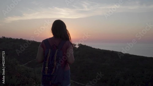 Woman with a backpack in a mountain watching the sunset in the sea.