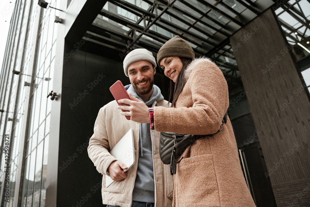 low angle view of freelancers in beanie hats looking at smartphone outside low angle view of freelancers in beanie hats looking at smartphone outside
