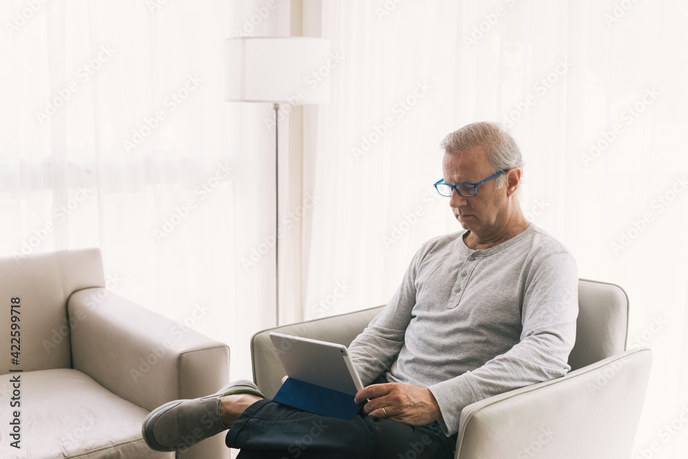 Old man in casual wear is looking a digital tablet in the living room.