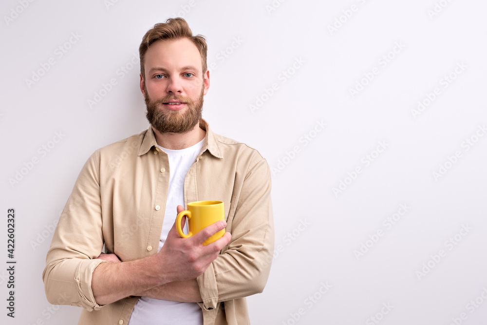 Young Caucasian Man In Casual Wear Posing At Camera Holding Yellow Mug In Hands Young Caucasian Man In Casual Wear Posing At Camera Holding Yellow Mug In Hands