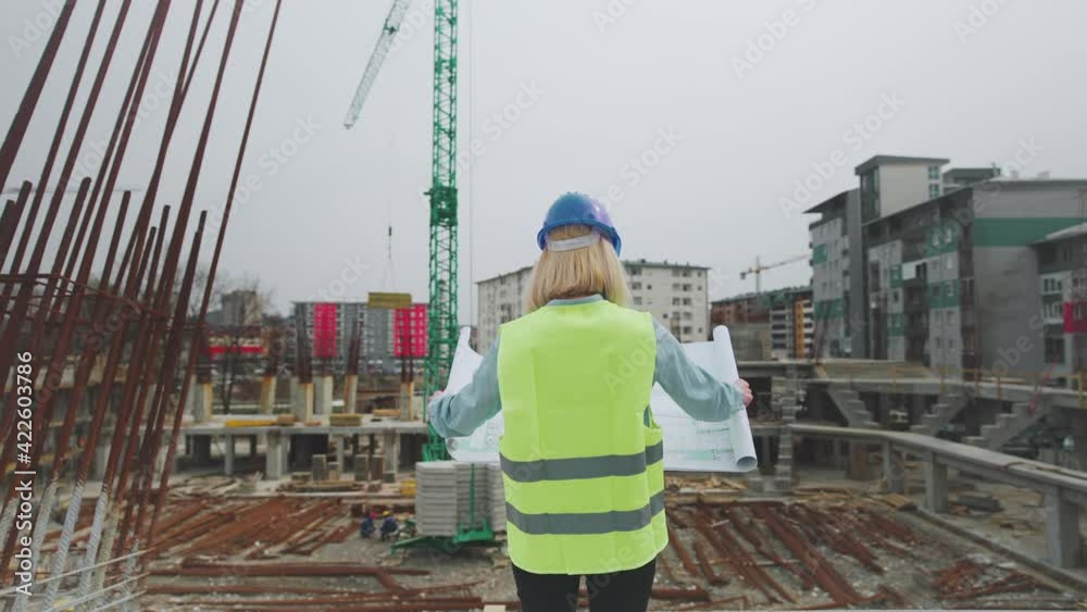 Overshoulder of an Architect observing the Commercial Construction Site and checking the Blueprints. Overshoulder of an Architect observing the Commercial Construction Site and checking the Blueprints.