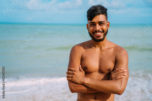 Athletic young latin american man on the beach with arms crossed. smiling man looking at camera