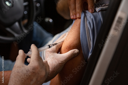 Homem idoso dentro do carro sendo vacinado por drive thru. photo