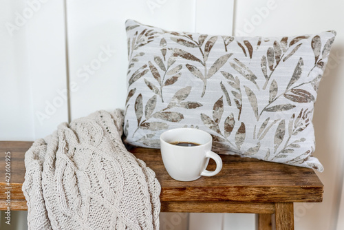 Cozy cup of coffee on a bench with a knitted blanket and pillow