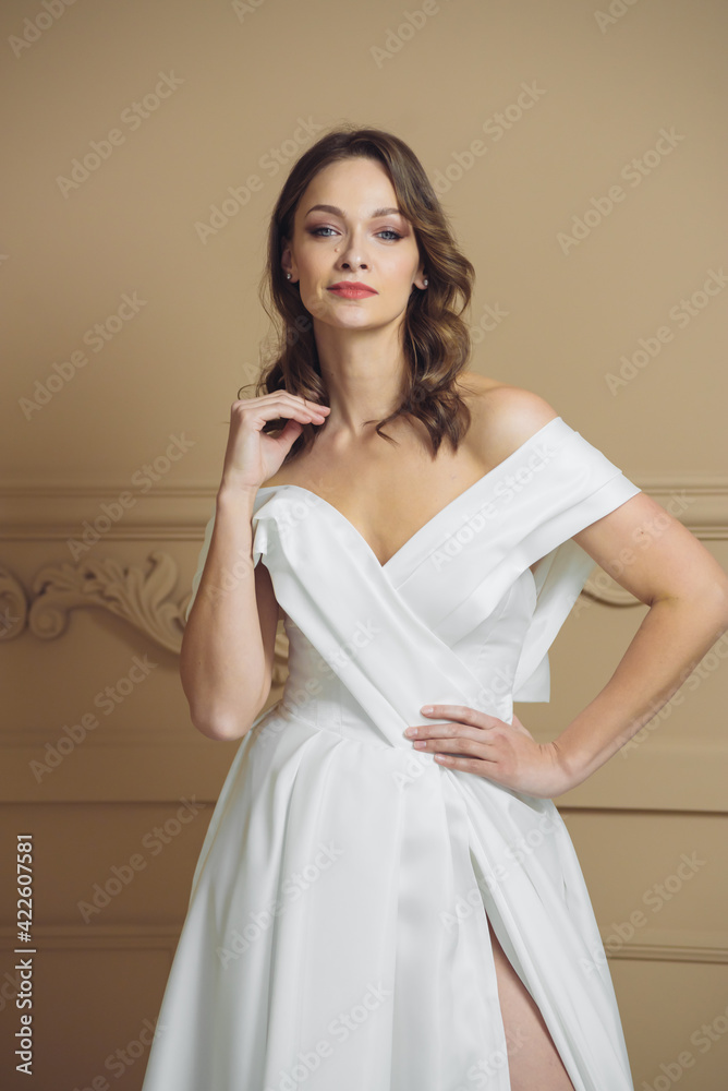 Beautiful bride in a beautiful wedding dress poses on the background of a hotel room Beautiful bride in a beautiful wedding dress poses on the background of a hotel room