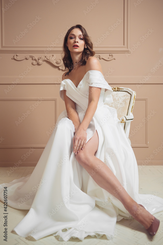 Beautiful bride in a beautiful wedding dress poses on the background of a hotel room Beautiful bride in a beautiful wedding dress poses on the background of a hotel room