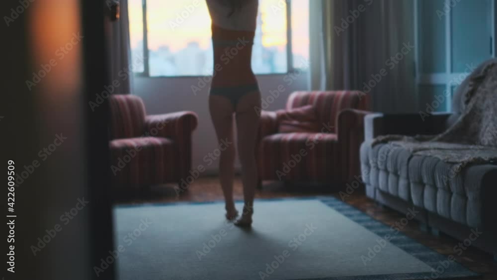 Woman takes off a dress. Young slim woman walks towards the window and takes off her dress