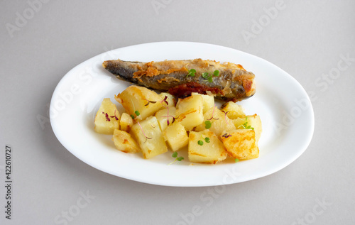 Fried fish and potatoes on a white plate on the table