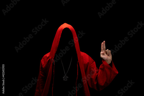 Mystery man in a red hooded cloak in the dark. Unrecognizable person. Hiding face in shadow. Pointing up with fingers. Ghostly figure. Sectarian. Conspiracy concept.

 photo