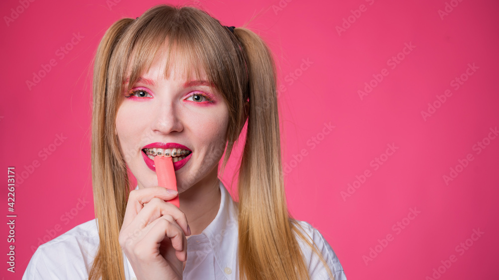 Portrait of a young woman with braces and bright makeup chewing gum on a pink background. Portrait of a young woman with braces and bright makeup chewing gum on a pink background.