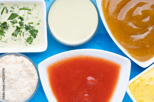 Different type of sauces in different white bowls on blue cement background photo