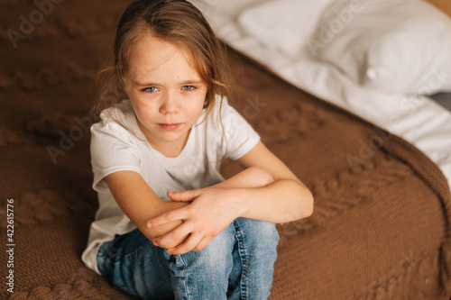 Φωτογραφία Top close-up view of distraught beautiful little girl with wet eyes from tears sits on bed in bedroom and looking at camera