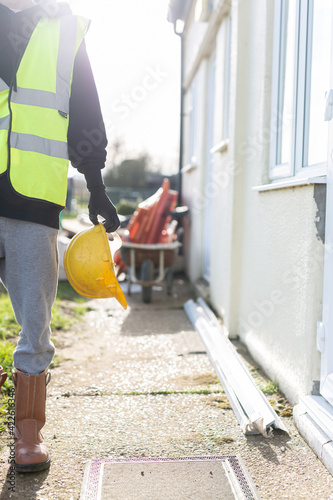 A close up of a unknown builder wearing a high visibility vest and holding a hard hat. Builder, safety, building site, laborer concept