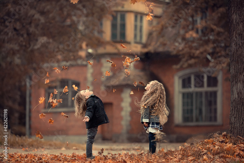 Beautiful long-haired blonde girl and a cute boy are throwing leaves up in autumn old park near the ivy-covered ancient mansion in Pushkin, Russia. Image with selective focus and toning. photo