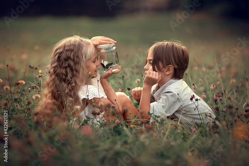 Beautiful long-haired girl and boy are looking at butterflies in the jar in summer park. Image with selective focus and toning