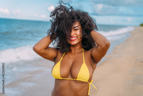 beautiful Latin American woman in bikini on the beach. Young woman enjoying her summer vacation on a sunny day, smiling, messing with her hair and looking at the camera