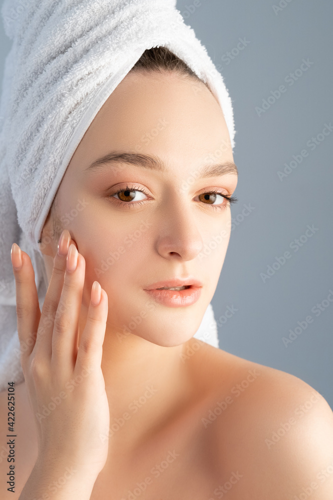 Facial skincare. Acne treatment. Health beauty wellness. Portrait of woman with nude makeup bare shoulders white towel on head touching flawless face skin after cleansing isolated on gray background. Facial skincare. Acne treatment. Health beauty wellness. Portrait of woman with nude makeup bare shoulders white towel on head touching flawless face skin after cleansing isolated on gray background.