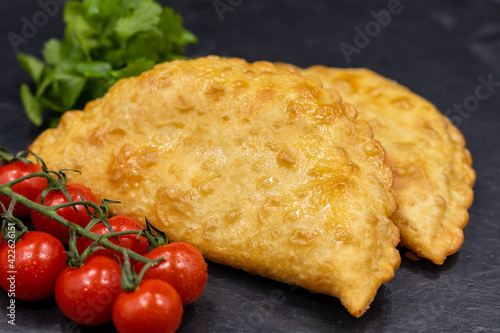 Chebureks on a black background. Served with coriander and cherry tomatoes. Caucasian cuisine.