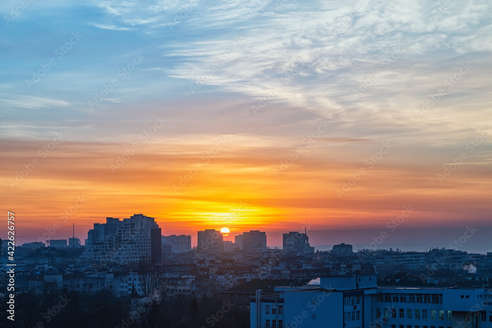 Sunrise over a small town. The rising sun turned the sky golden orange. Dawn fire in the sky over a small city. Cityscape at early morning. Scenic landscape at sunrise.