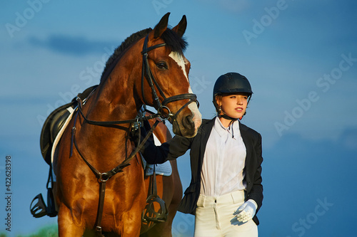 Beautiful horse rider girl stands near a horse on a farm   © Rakursstudio