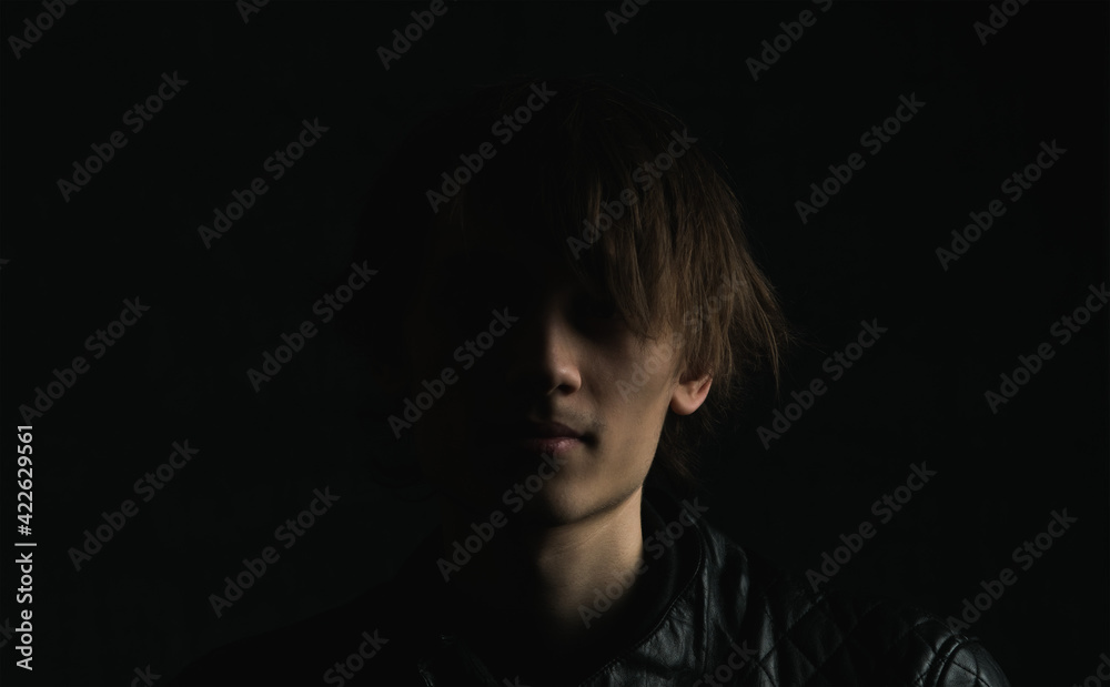 Portrait image of a young guy with long hair on a very dark background Portrait image of a young guy with long hair on a very dark background