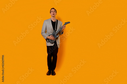 stylish and cool guy in a suit and with a game guitar on a yellow background, © Alexander