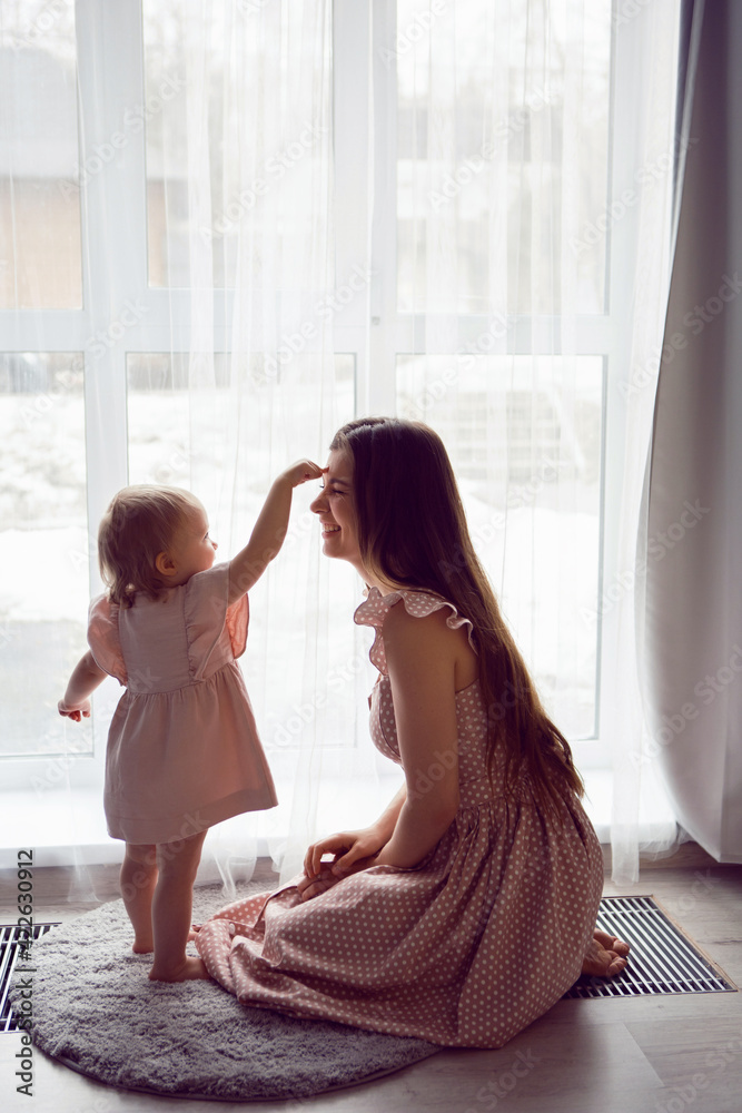 woman with a girl child in pink dresses stands at a large window