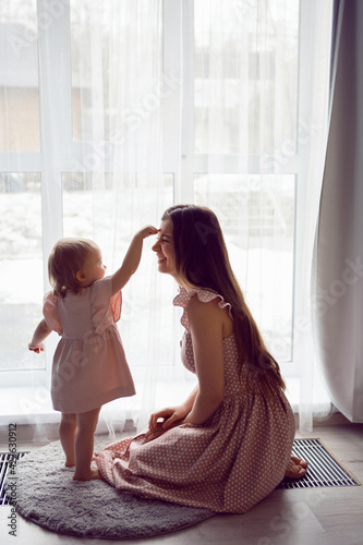 Obraz na płótnie woman with a girl child in pink dresses stands at a large window w salonie