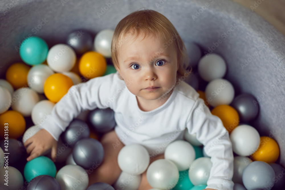 girl child sits in a pool with colorful plastic balls girl child sits in a pool with colorful plastic balls