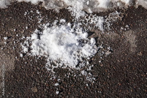 A crushed snowball with an imprint of the sole on the asphalt. Melting snow in spring © akintevs