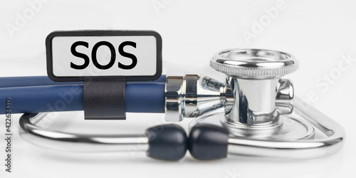 On the white surface lies a stethoscope with a plate with the inscription - SOS