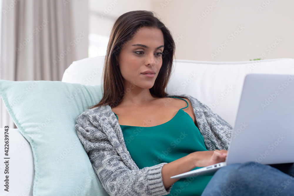 Caucasian woman sitting on a couch using laptop and smiling Caucasian woman sitting on a couch using laptop and smiling