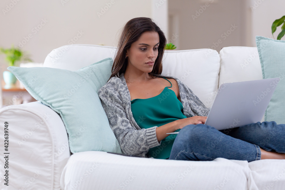 Caucasian woman sitting on a couch using laptop and smiling Caucasian woman sitting on a couch using laptop and smiling